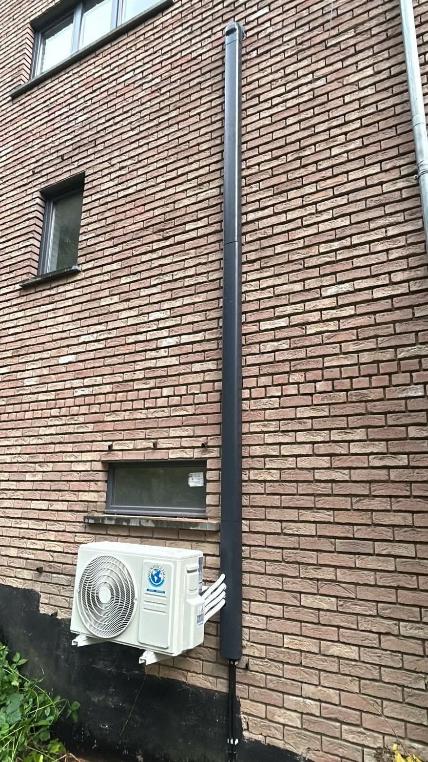 Unité extérieure de climatisation et goulotte verticale installées sur une façade en briques