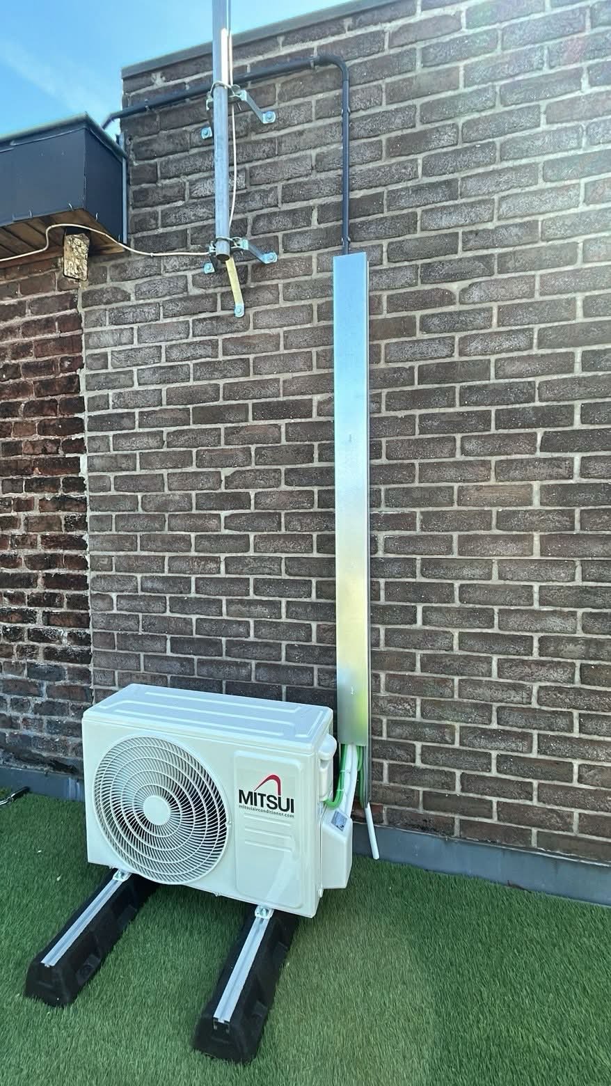 Unité extérieure de climatisation posée sur supports au pied d’une façade